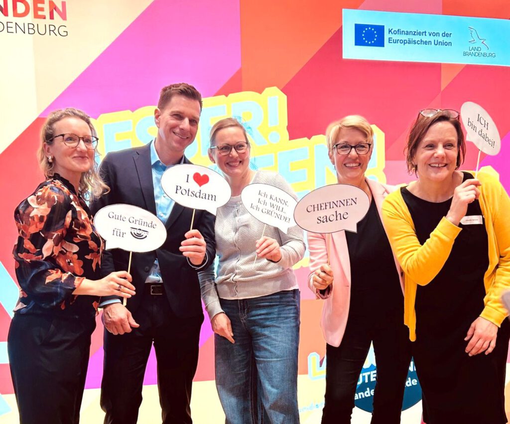 Teilnehmende beim Netzwerkformat „Frauen auf dem Weg“ in Potsdam – Gründerinnen und Unternehmerinnen zeigen Statementschilder vor einer farbigen Eventkulisse. Motiv für Beitrag zu Sichtbarkeit, Austausch und Female Entrepreneurship in Potsdam.