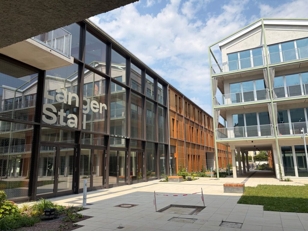 Außenansicht des Langen Stalls im Kreativ Quartier Potsdam mit Glasfassade, Holzfassade und modernem Innenhof.